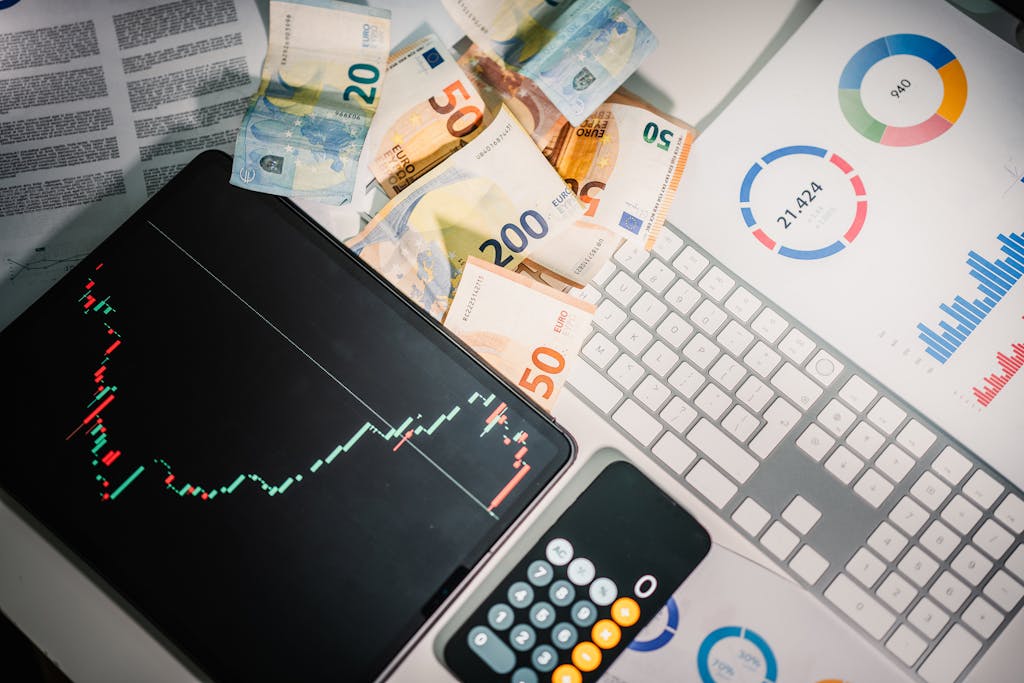 Overhead view of financial tools with Euro banknotes on a desk showing market trends and graphs.