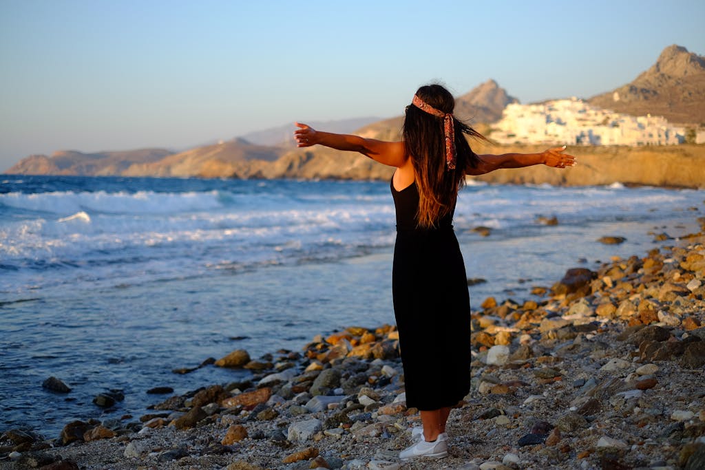 Woman enjoying freedom at sunset on a rocky beach in Greece.